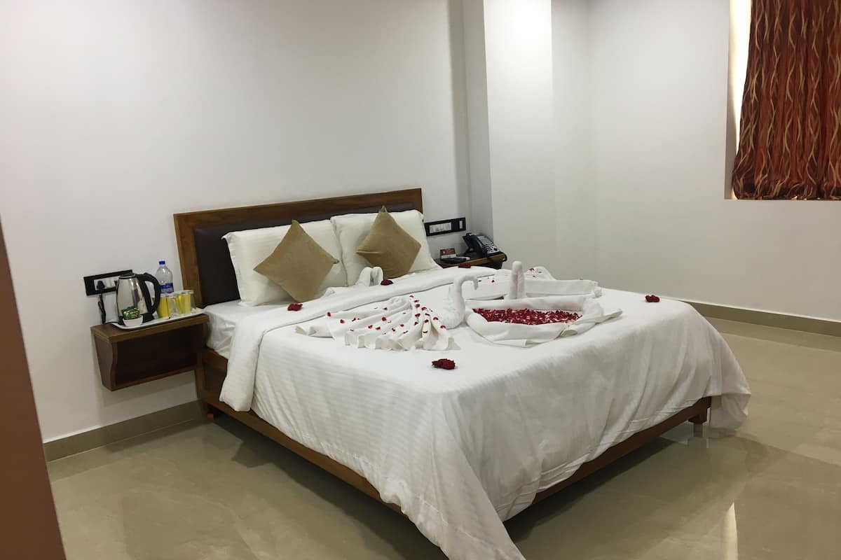 A neatly made bed with white linens, a wooden headboard, and decorative pillows. There is a bedside table with a phone, a water bottle, and a small plant.