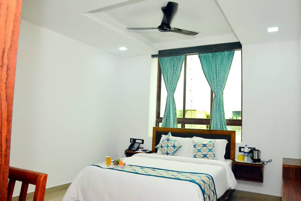A hotel room with a bed, a nightstand, a chair, a ceiling fan, and a window with curtains.