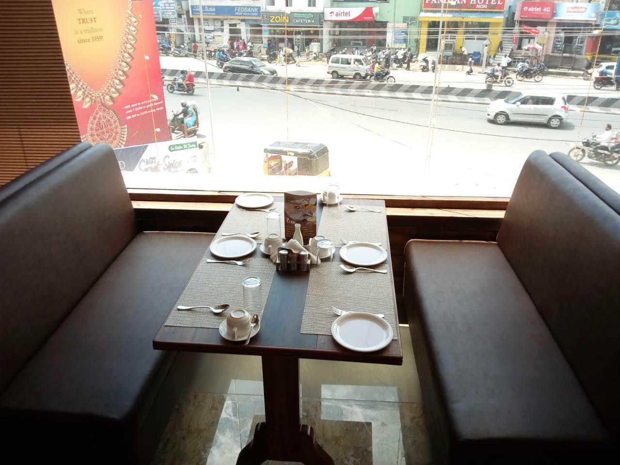 A dining area with a table set for two, a window view of a busy street, and a sign for a hotel in the background.