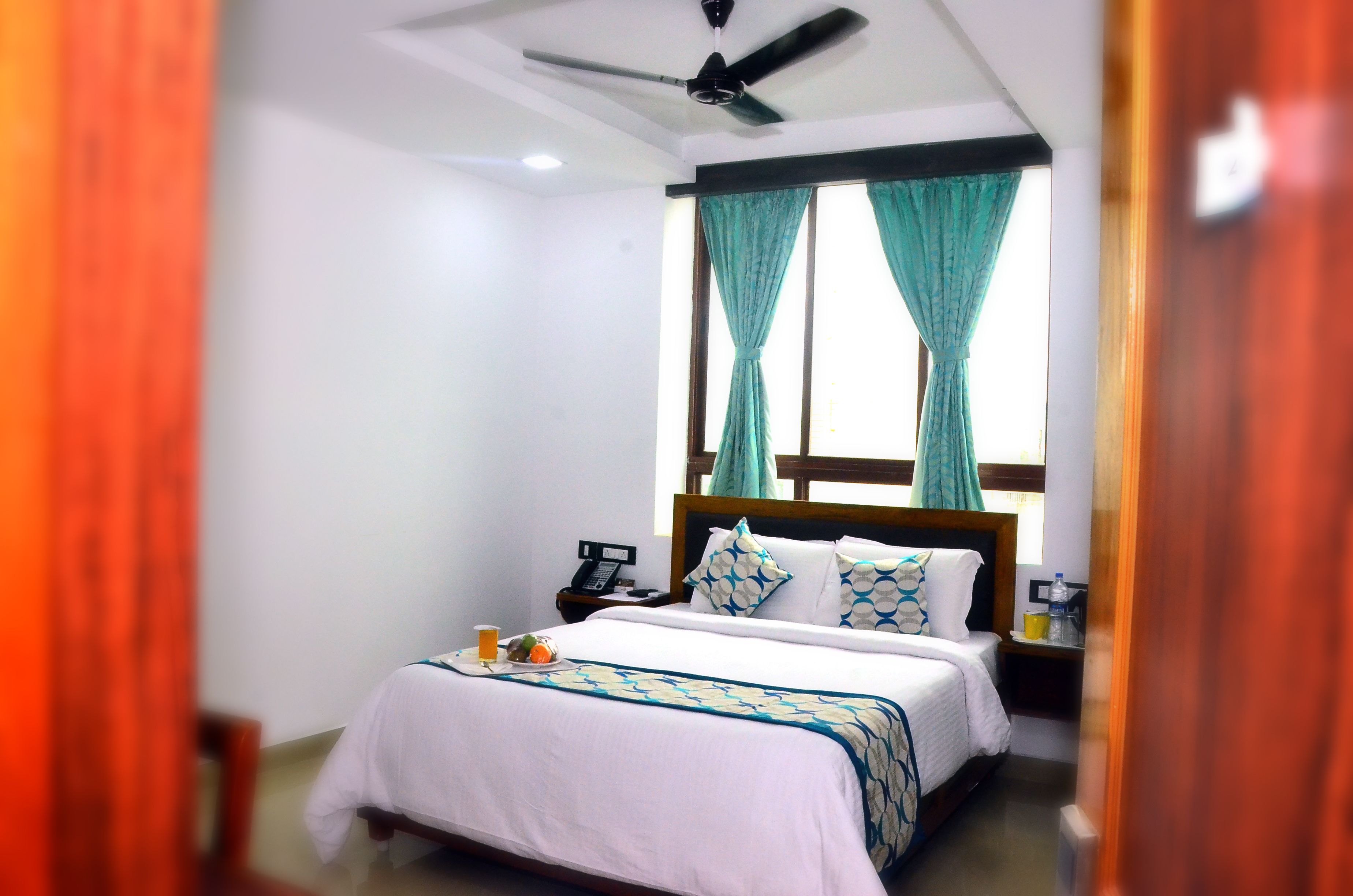 A hotel room with a bed, a ceiling fan, a bedside table with a phone, and curtains on the window.