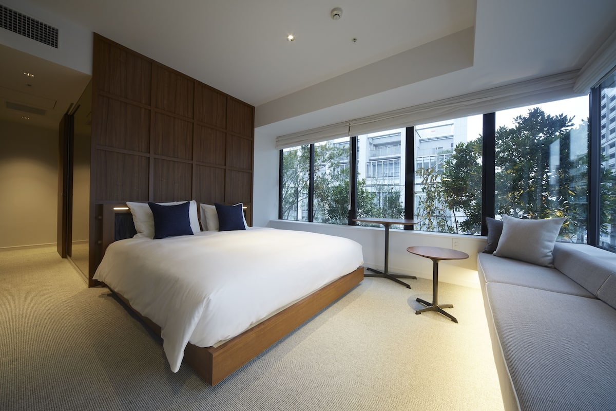 Un dormitorio moderno con una cama grande, un área de descanso y vistas a la ciudad a través de amplios ventanales.