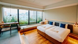 Una habitación de hotel moderna con una cama grande, un escritorio y vistas de la ciudad a través de amplios ventanales.