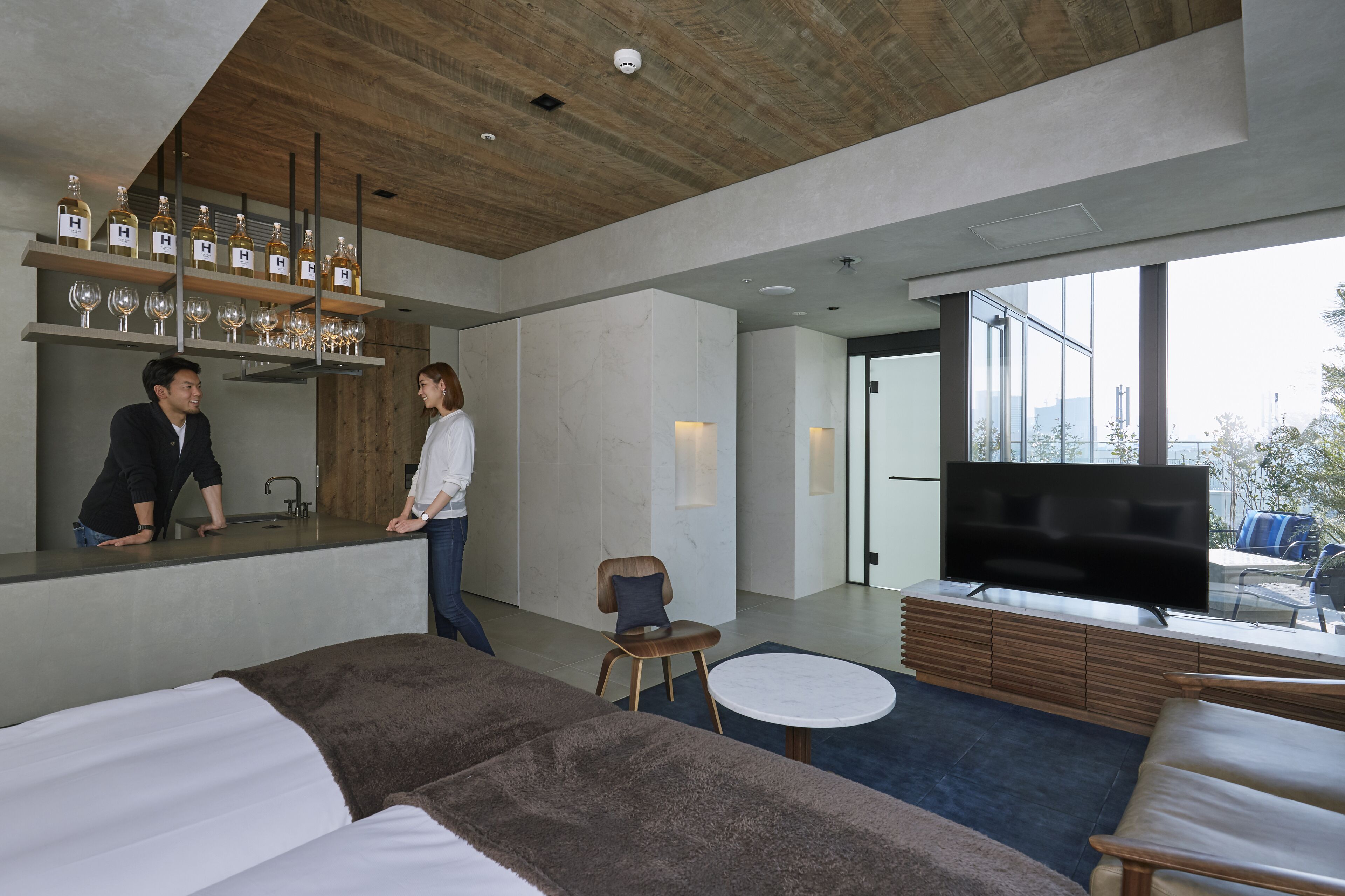 A modern hotel room with a bar area, a large flat-screen TV, and a view of the city.