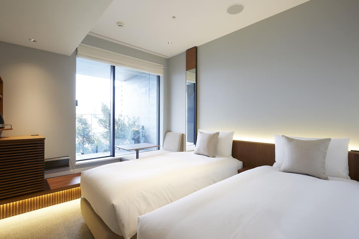 Una habitación de hotel moderna con dos camas, un ventanal grande y una mesita de noche de madera.