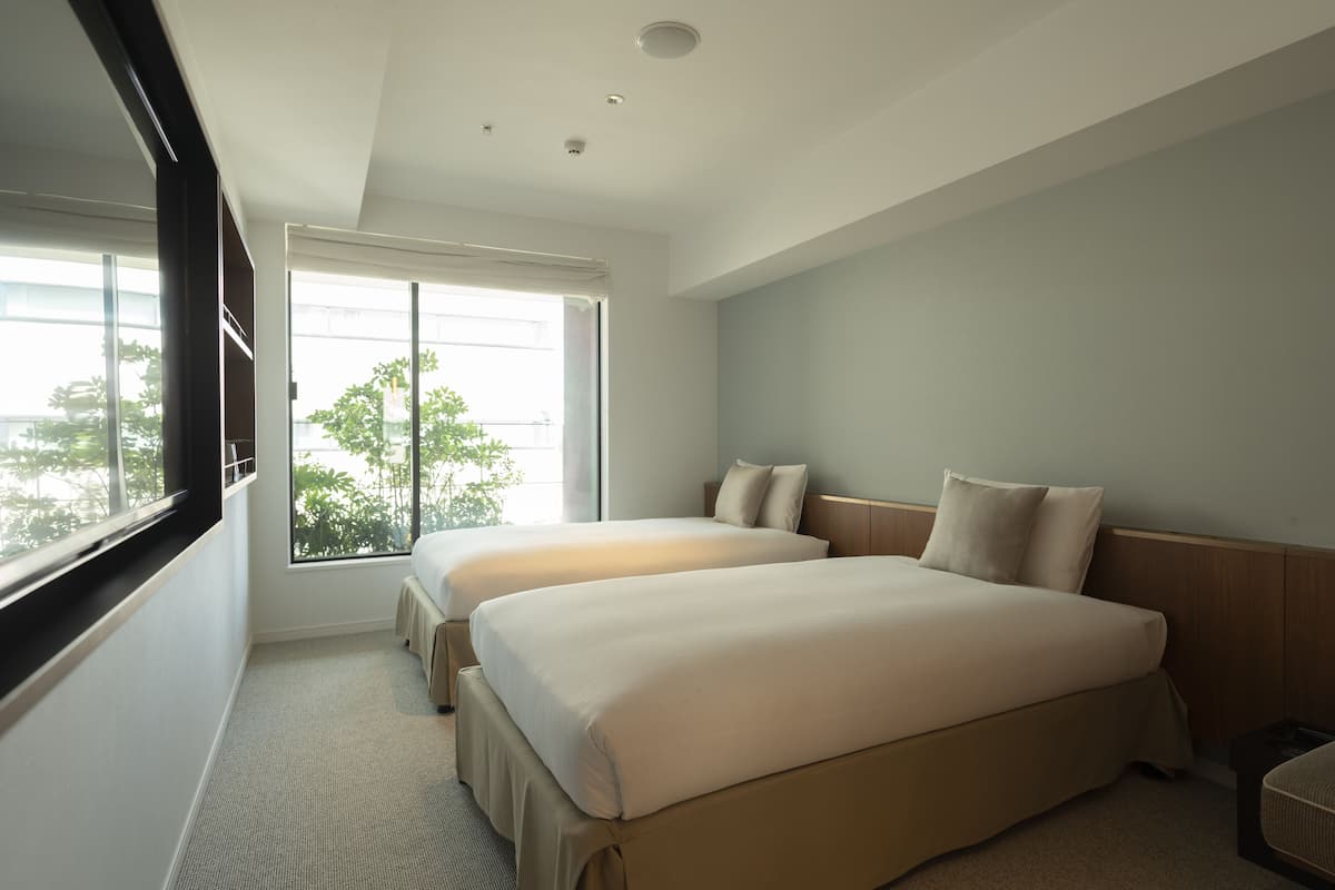 Habitación de hotel con dos camas, un ventanal con vistas a zonas verdes e iluminación empotrada en el techo.