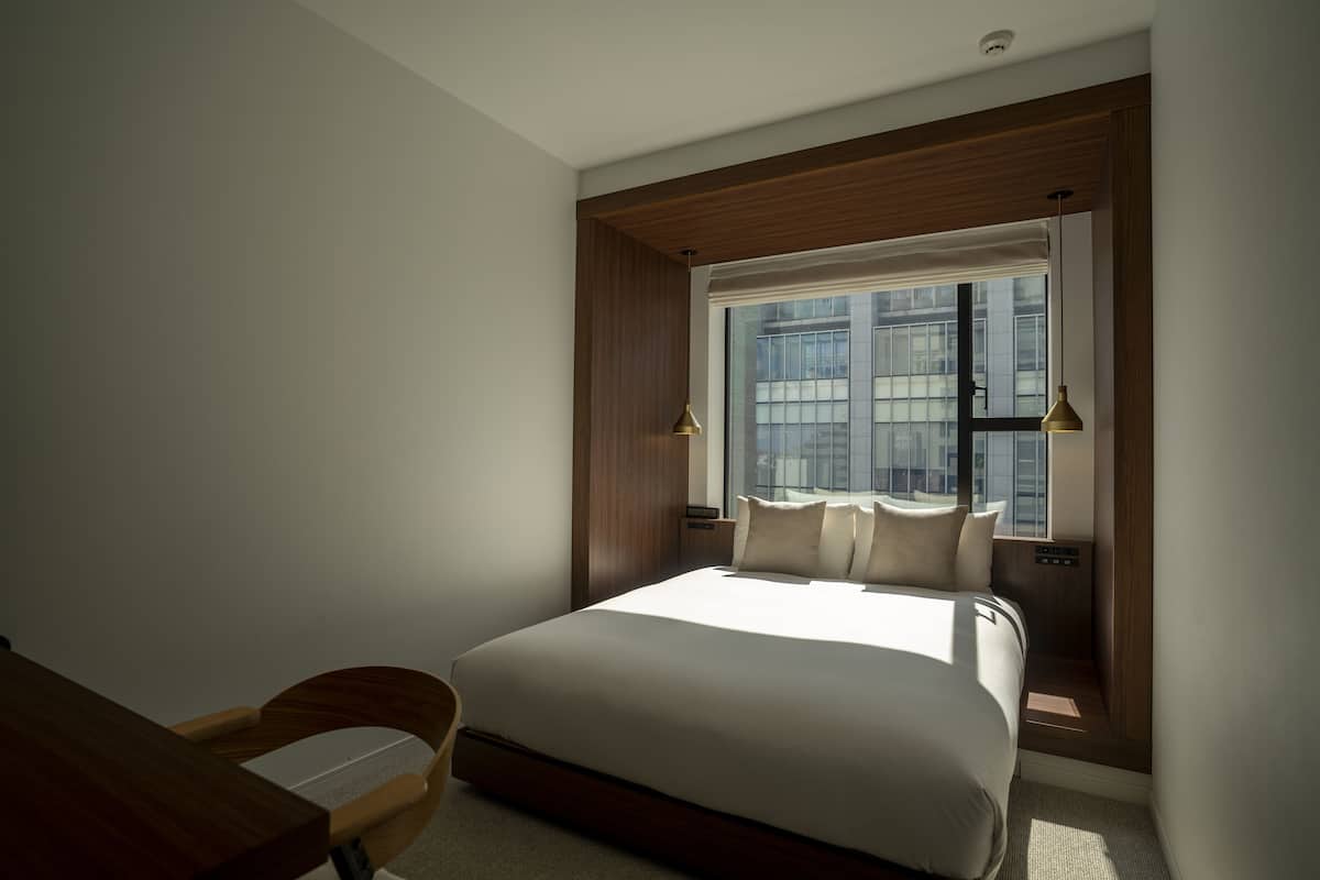 Un dormitorio moderno con una cama grande, cabecera de madera y ventana con vistas a la ciudad.