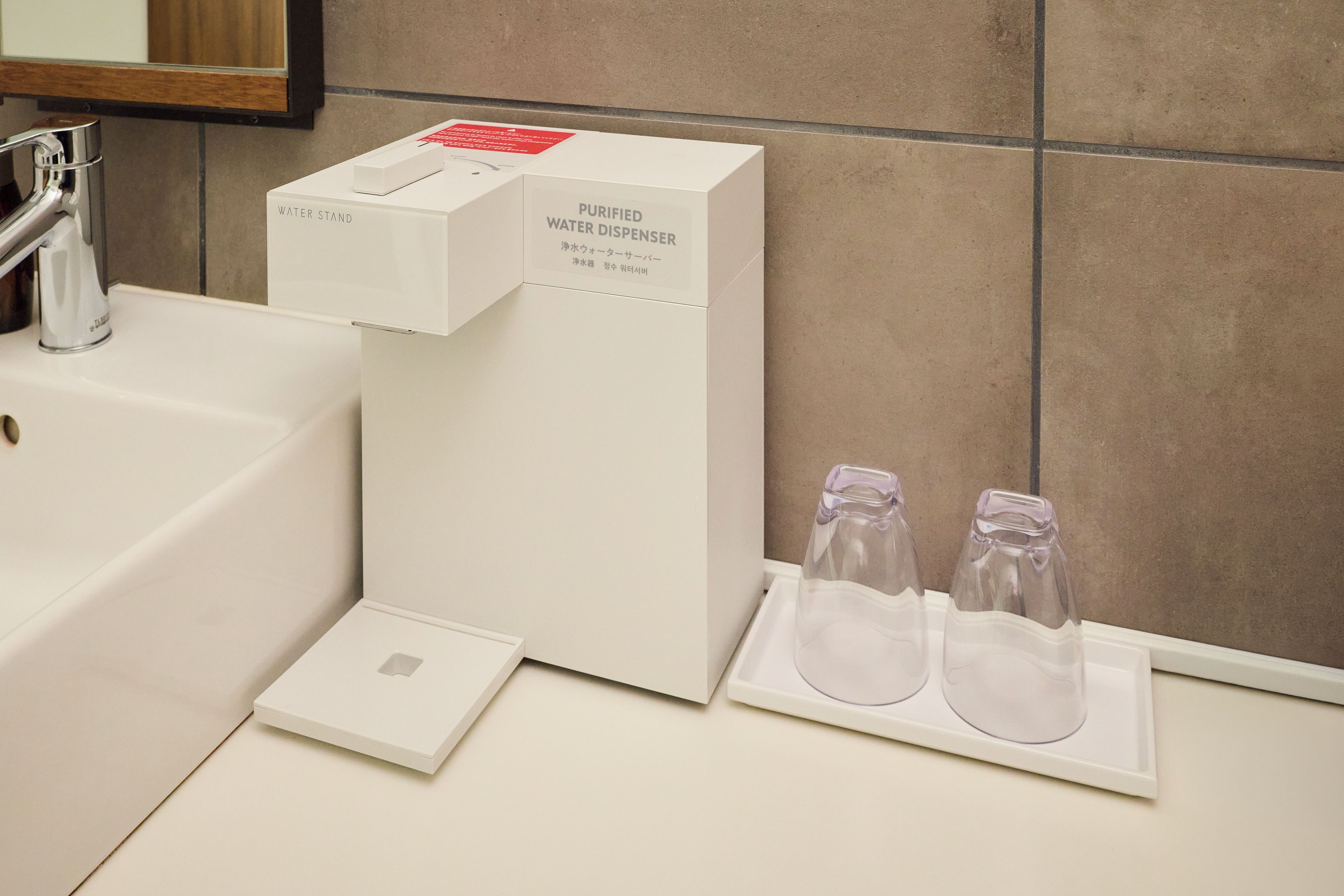 A bathroom with a white water dispenser, a faucet, and two empty glass bottles on a tray.