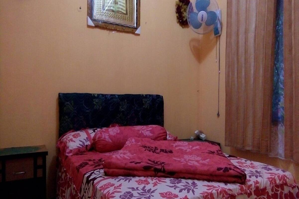 Une chambre à coucher comprenant un lit, une table de chevet, une étagère fixée au mur et une fenêtre avec des rideaux.