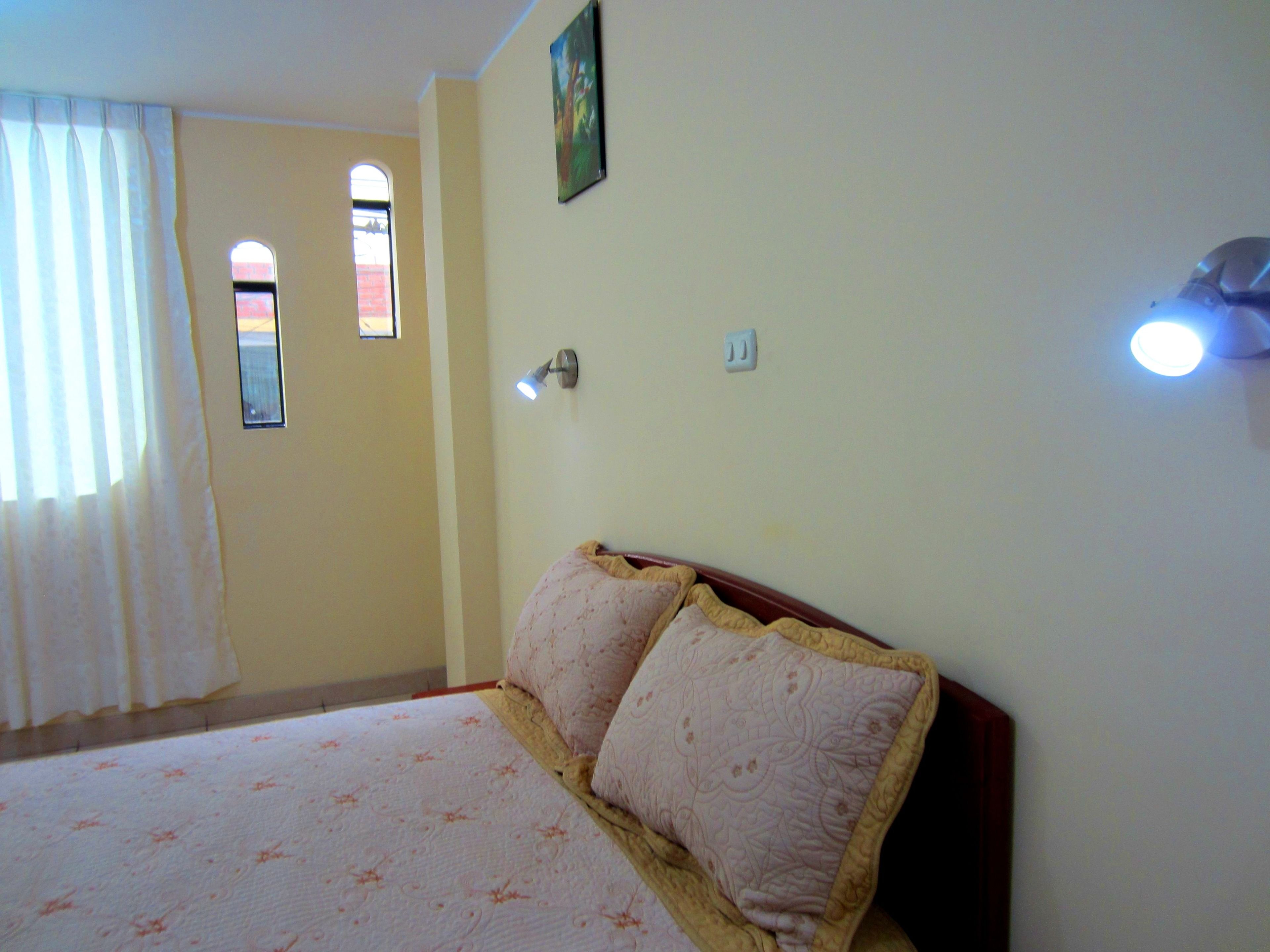 Un dormitorio con cama, ventana y una lámpara fijada a la pared.
