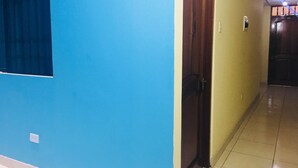 A hallway with a blue wall, a wooden door, and a tiled floor. - Hostal Sandel (Barranca)