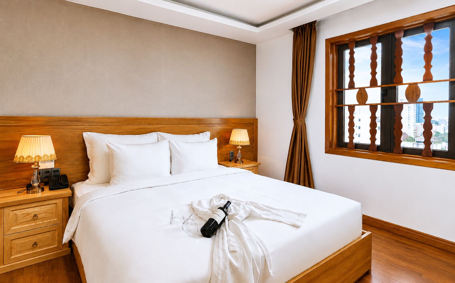 A hotel room with a large bed, two bedside tables with lamps, a wooden headboard, a window with a view, and a neatly made bed with a robe and wine bottle.