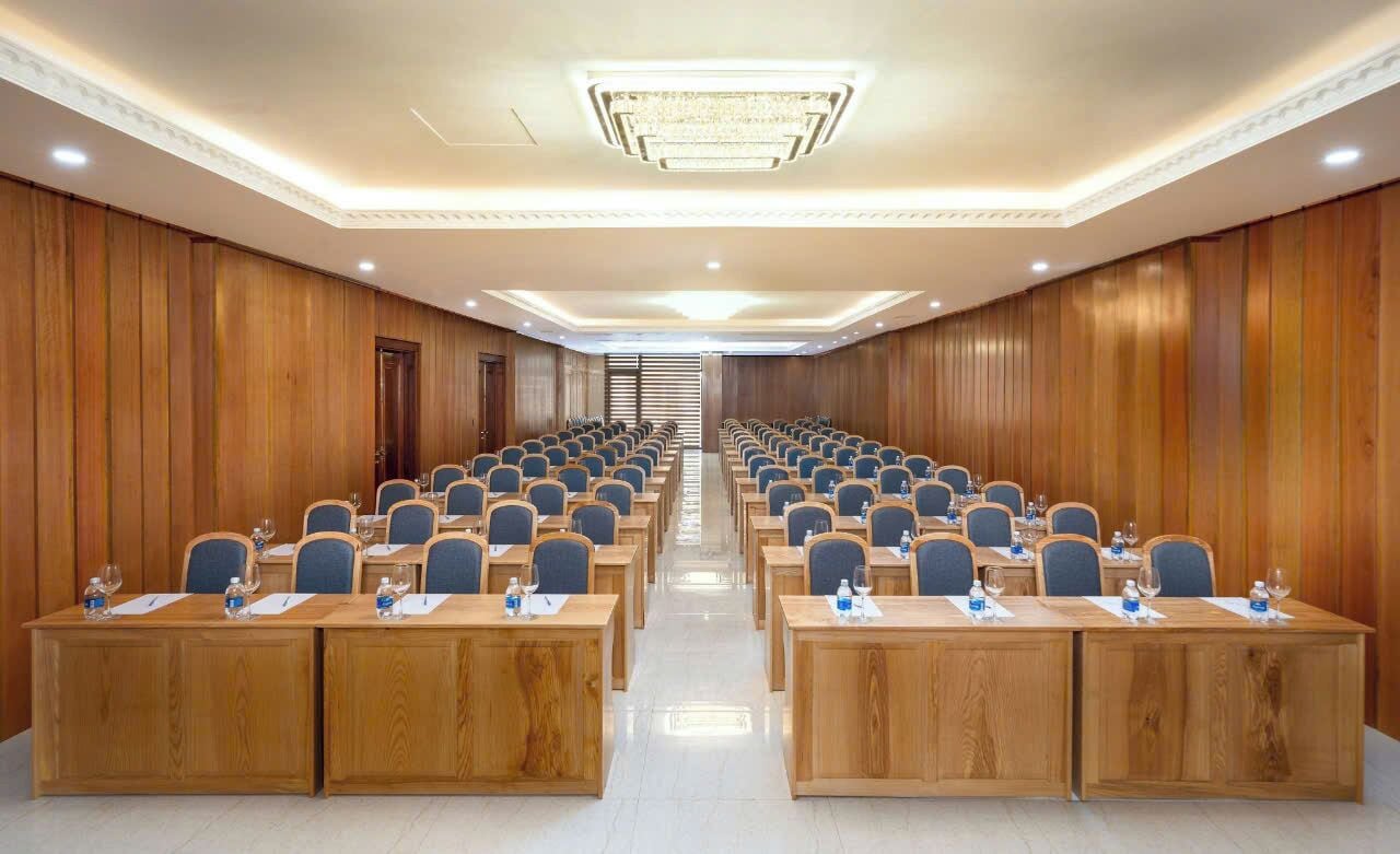 Konferenssitila, jossa on riveissä pöytiä ja tuoleja, seinät on verhoiltu puupaneloinnilla ja katosta roikkuu koristeellinen kattokruunu.