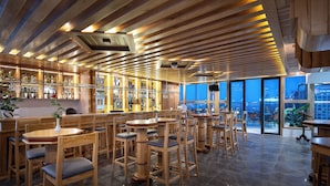 A restaurant with wooden furniture, a bar area, and large windows offering a city view.