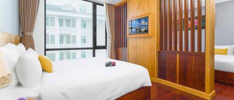 Habitación de hotel con una cama grande, un separador de madera, una ventana con vistas a un edificio y un cuadro en la pared.