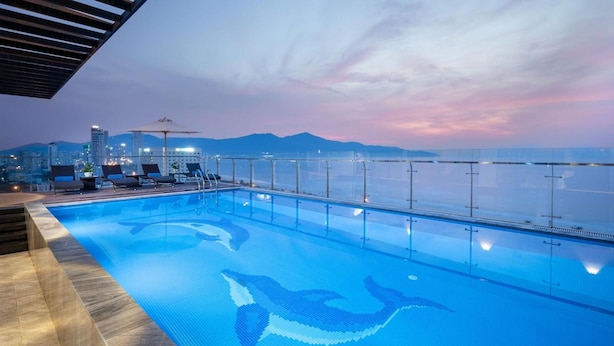 A rooftop infinity pool with a cityscape and mountains in the background.