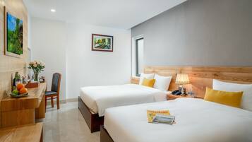 A hotel room with two beds, a desk with a chair, a vase of flowers, and a painting on the wall.
