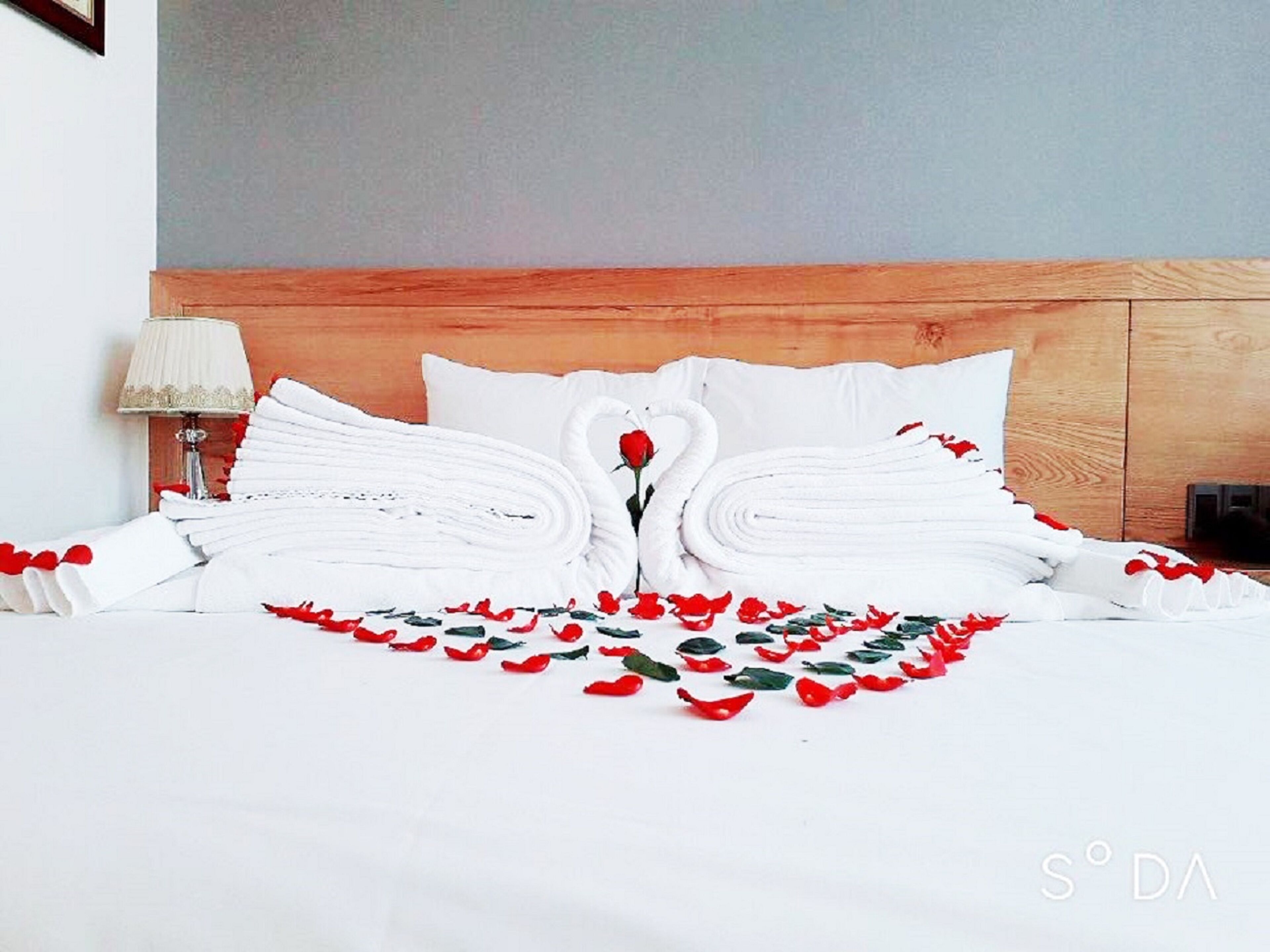 A neatly made bed with white linens and a rose-shaped towel arrangement.