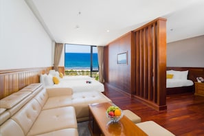 A hotel room with a large bed, a sofa, a dining table with fruit, and a view of the beach. - Sunny Ocean Hotel & Spa (Da Nang)