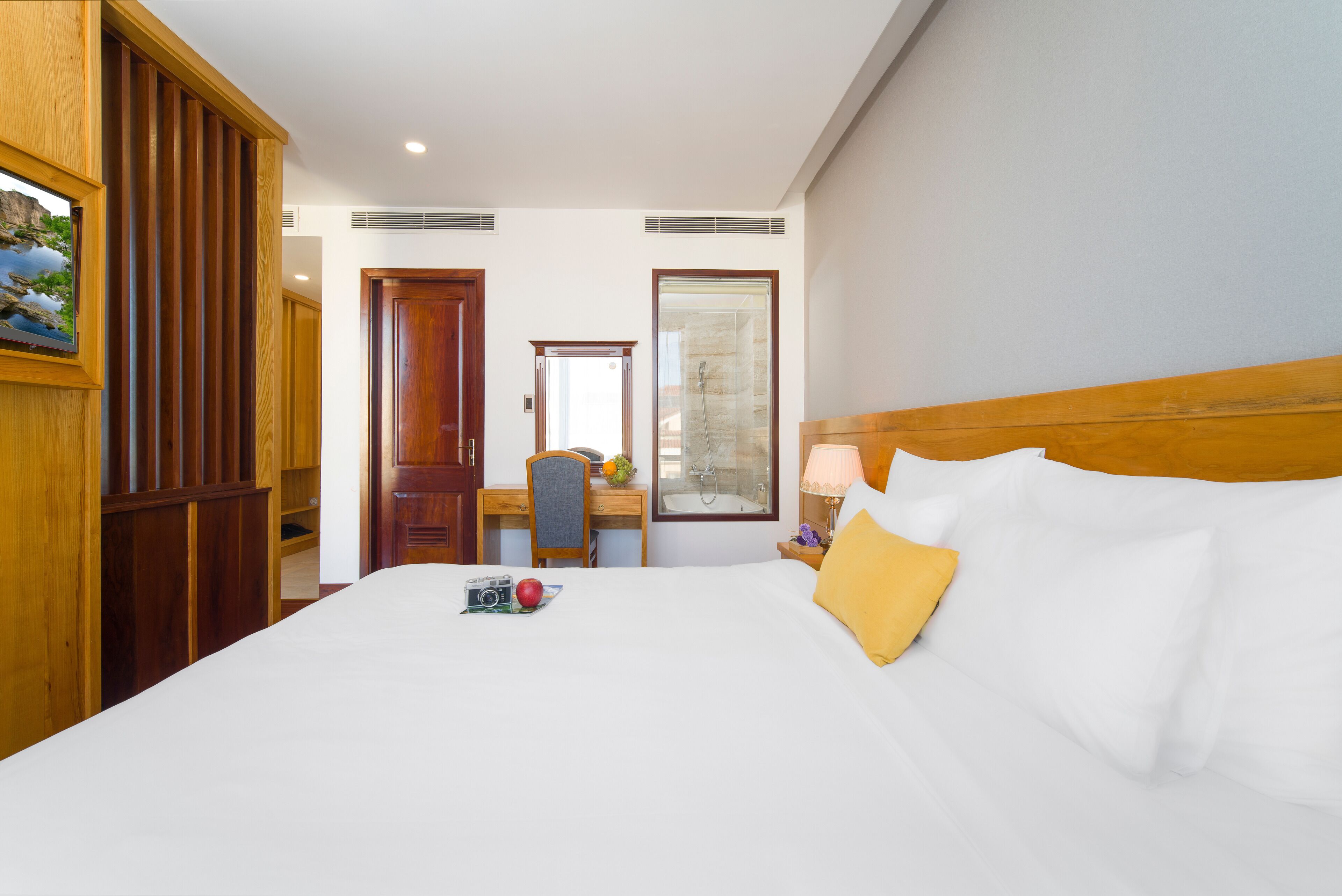 Ein Hotelzimmer mit einem großen Bett, einem Holzschrank, einem Schreibtisch mit Stuhl, einem Badezimmer mit Spiegel und einem Nachttisch mit Lampe.