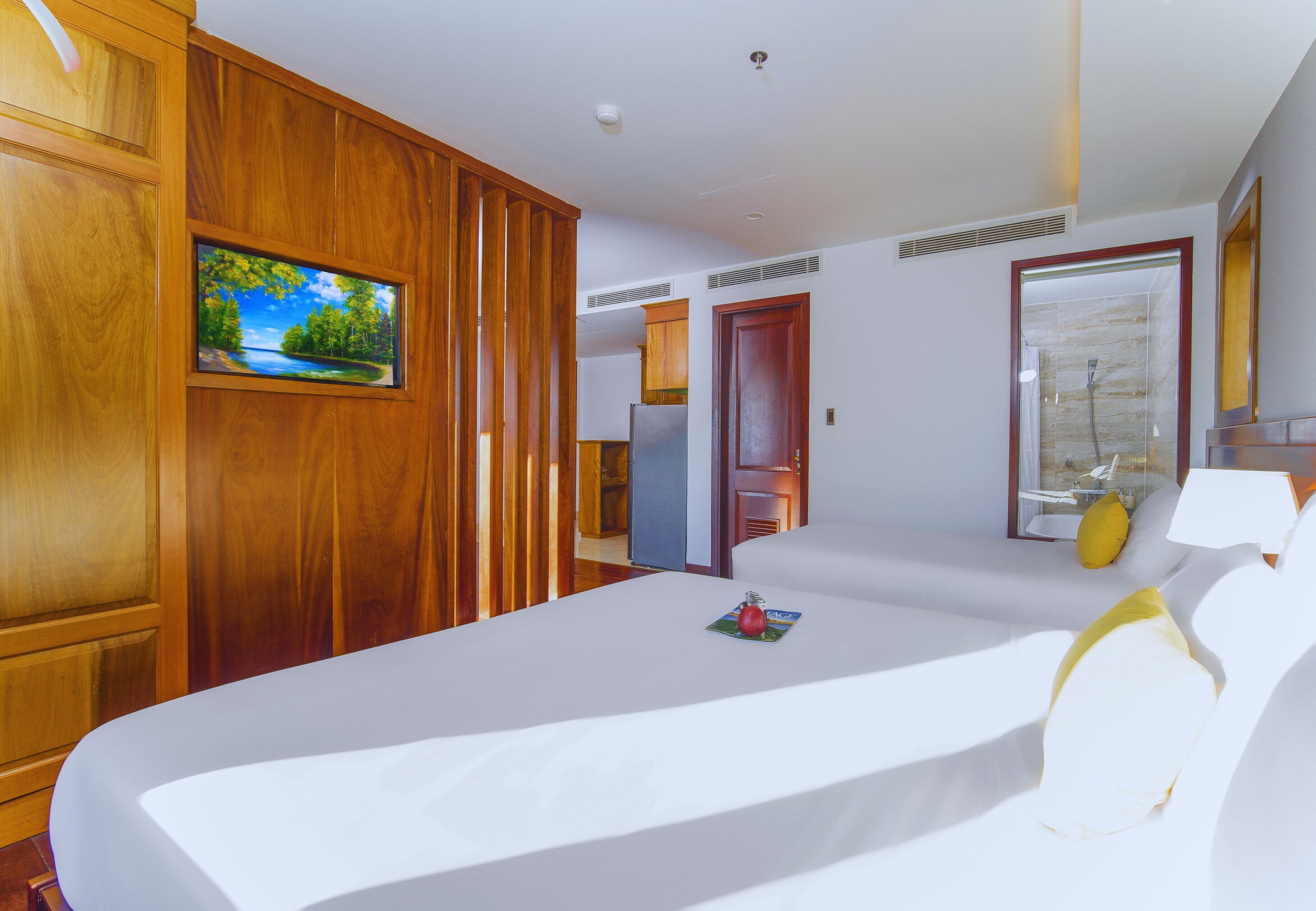 Habitación de hotel con una cama grande, paneles de madera, televisor y baño con ducha de vidrio.
