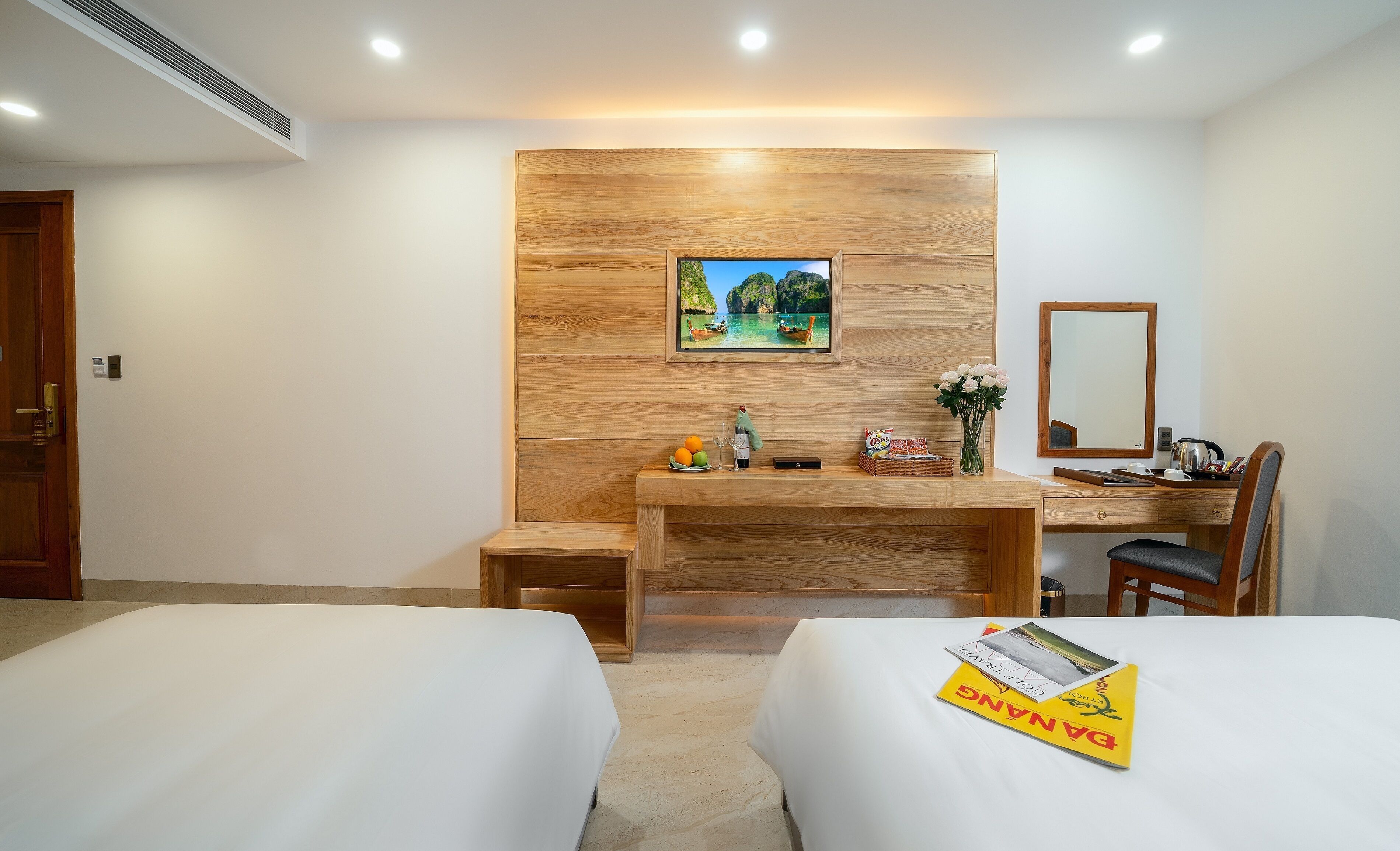 Hotelkamer met twee bedden, een houten bureau met een computer, een spiegel en een lijst met een afbeelding aan de muur.