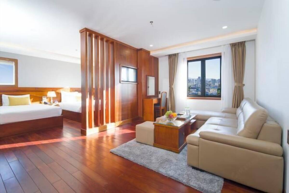 A hotel room with a bed, sofa, and a desk with a lamp.