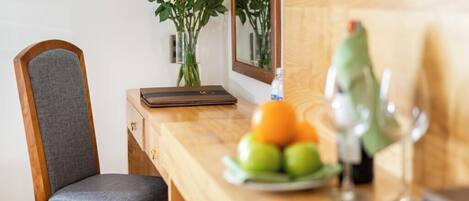 Een houten stoel met een grijze kussen, een houten bureau met een bloemenvaas, een schaal fruit, en een wijnglas.