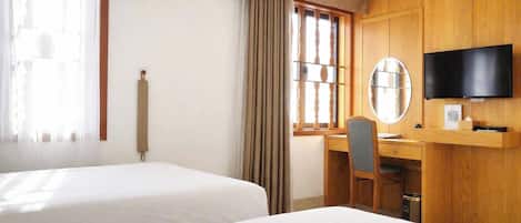 Habitación de hotel con dos camas, un escritorio, una silla, un televisor y un ventanal con cortinas.