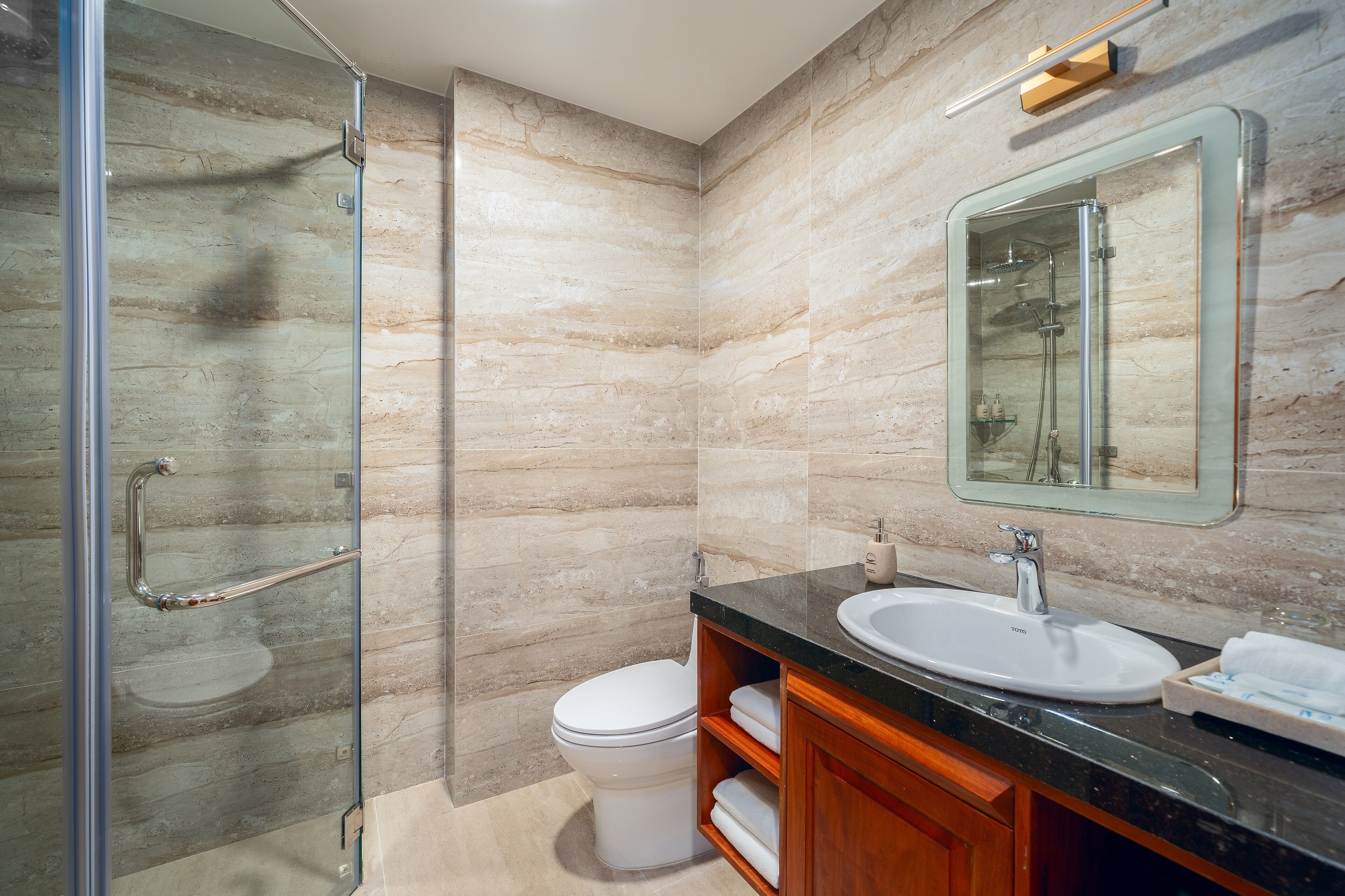 A modern bathroom with a glass shower enclosure, a white toilet, a sink with a mirror, and wooden cabinetry.