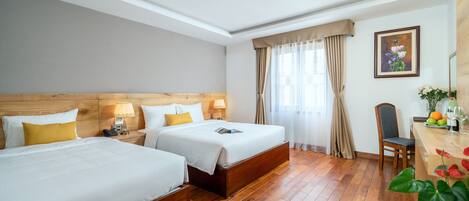 Une chambre d’hôtel avec deux lits, des têtes de lit en bois, un bureau avec une chaise, un vase avec des fleurs et un tableau au mur.
