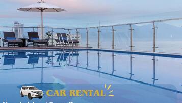 Un espace aménagé au bord de la piscine avec des chaises longues et un parasol, la possibilité de louer une voiture privée pouvant accueillir jusqu'à sept personnes, et une vue sur les montagnes en arrière-plan.