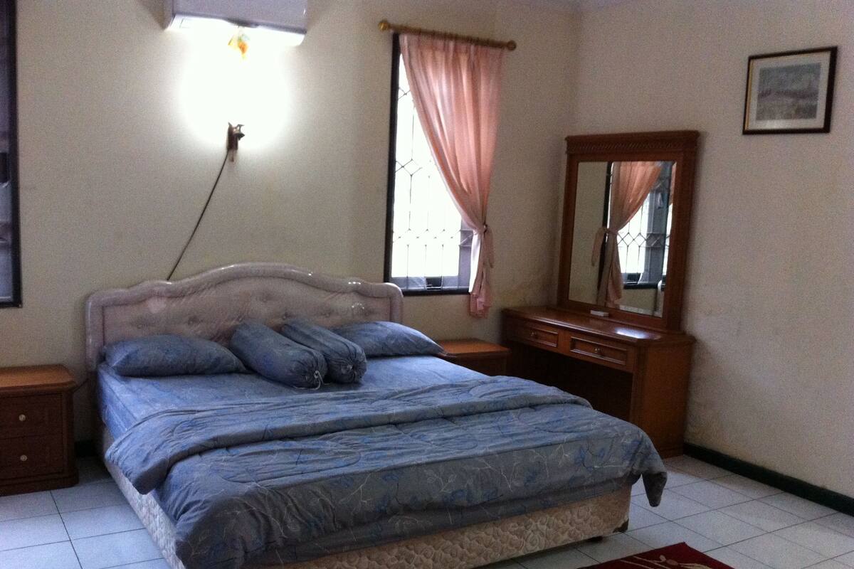 A bedroom with a bed, a nightstand, a dresser, a mirror, and a window with curtains.