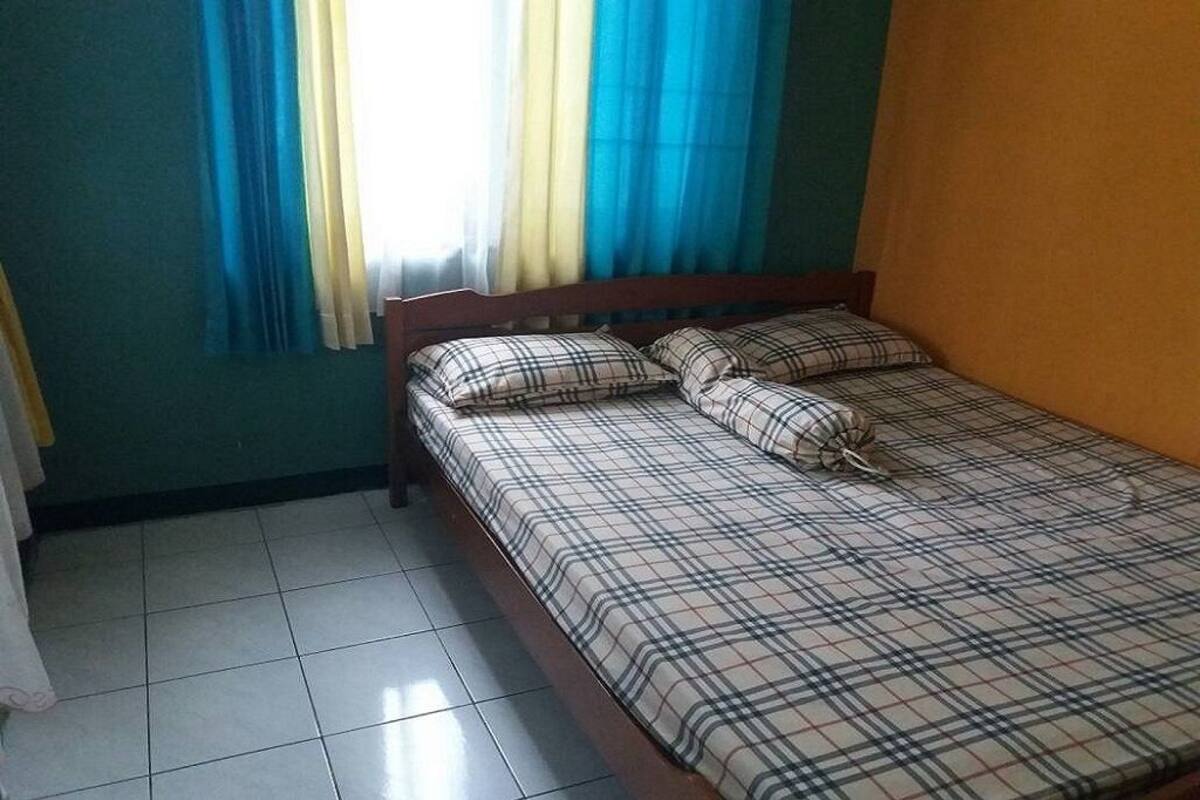 A single bed with plaid bedding in a room with teal walls and a window with blue and yellow curtains.