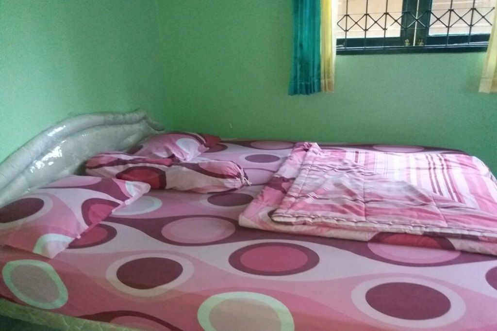 Una cama con colcha y almohadas a lunares, una ventana con rejas y una pared verde.