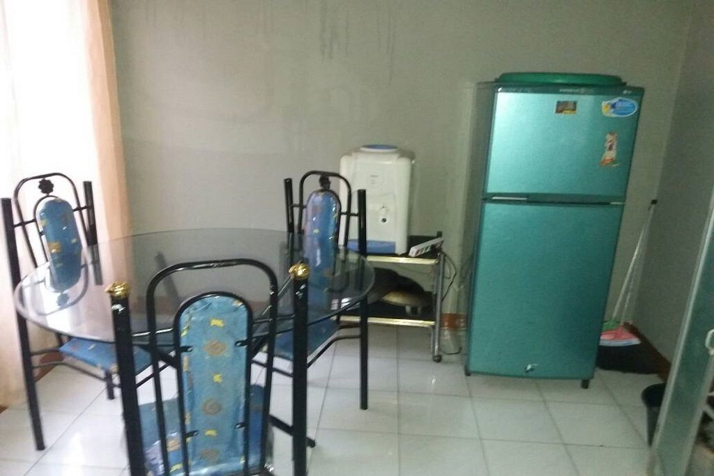 Une petite cuisine avec une table ronde, deux chaises, un réfrigérateur et un distributeur d’eau.