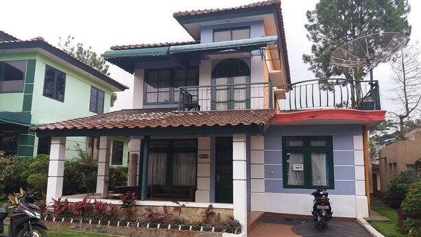 Un edificio de dos pisos con techo de tejas, un balcón y un pequeño jardín.