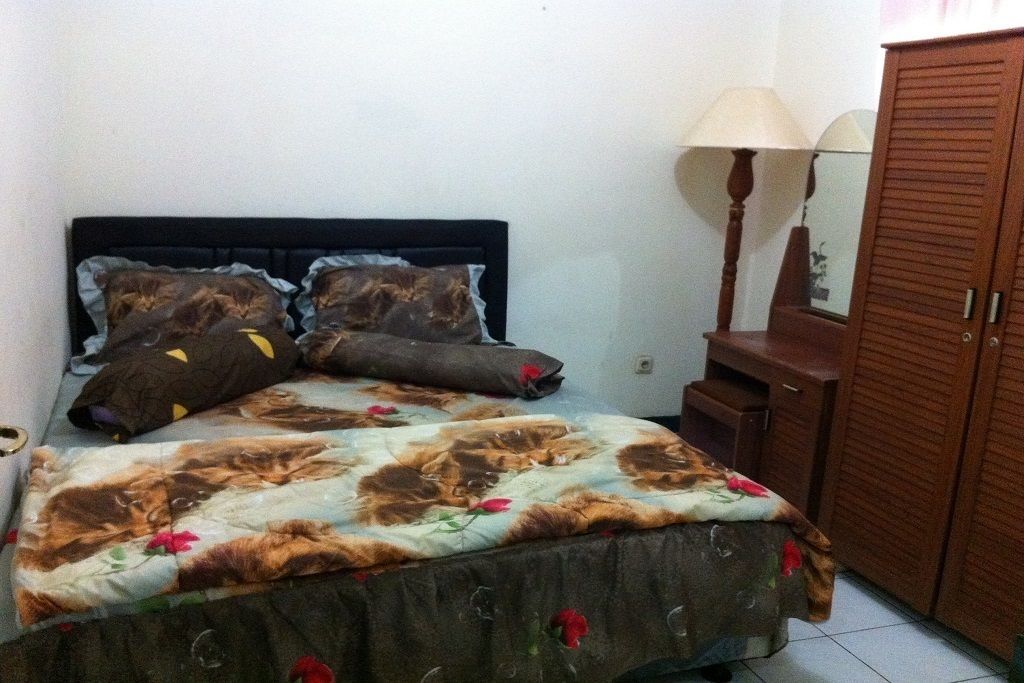 Una camera da letto con un letto, cuscini, un comodino, una lampada e un armadio.