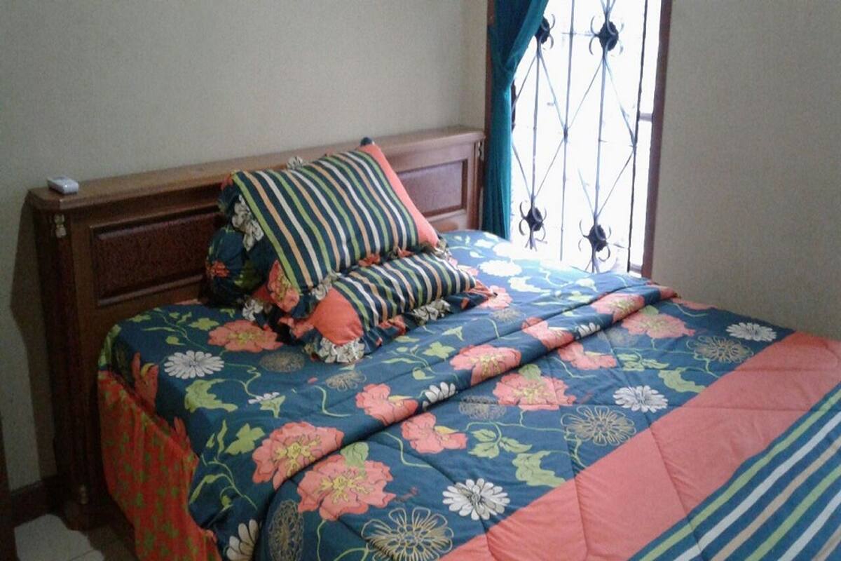 Una cama con ropa de cama floral y almohadas a rayas, un cabecero de madera y una ventana con barrotes.
