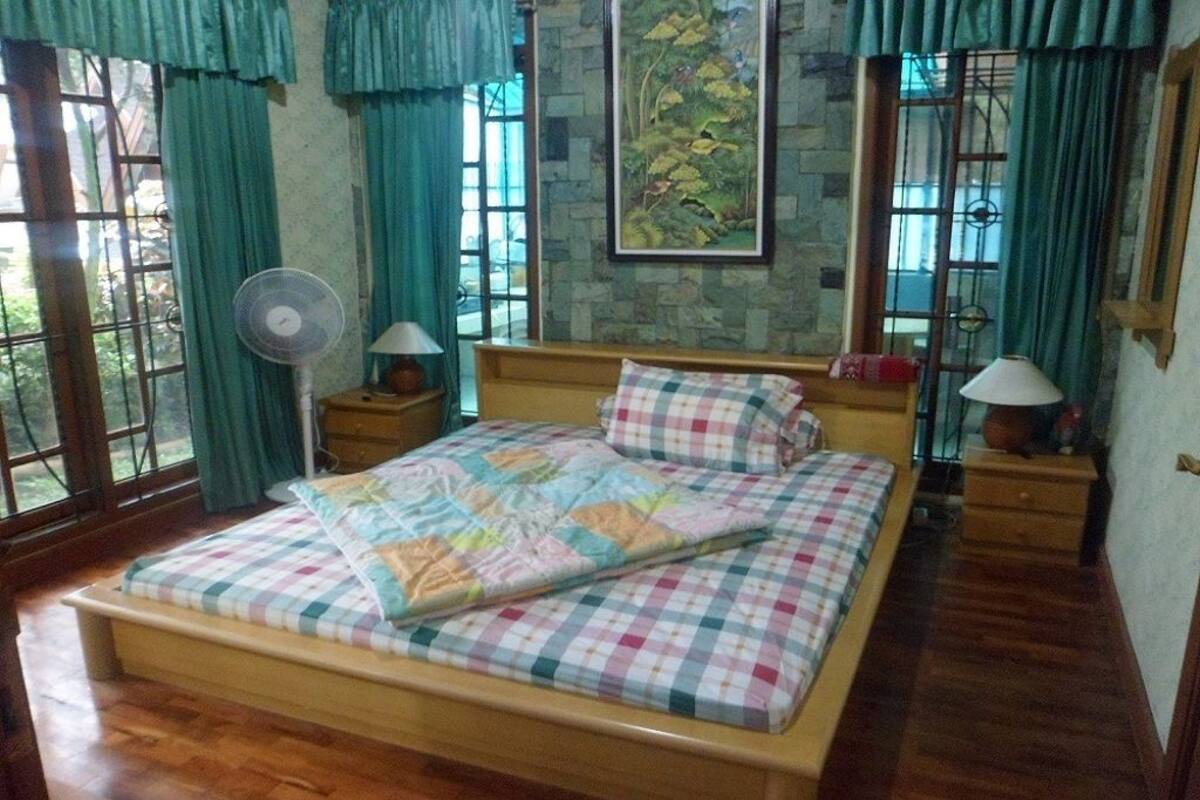 Un dormitorio con una cama de madera, una pared de piedra y un ventanal con cortinas.