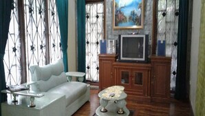 A living room with a white sofa, a small round table, a cabinet with a television, and a decorative piece on the floor.