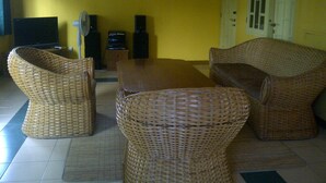 A room with yellow walls, a television, speakers, and wicker furniture.