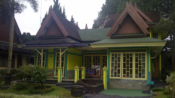 A traditional building with a green roof and yellow trim, surrounded by well-maintained gardens.