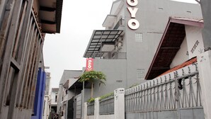 Eine schmale Straße mit einem Gebäude, das ein großes 'OYO'-Schild, einen Metallzaun und einen Baum zeigt.