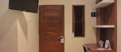 A room with a wooden door, a mounted TV, a small window, and a wooden desk with a chair.