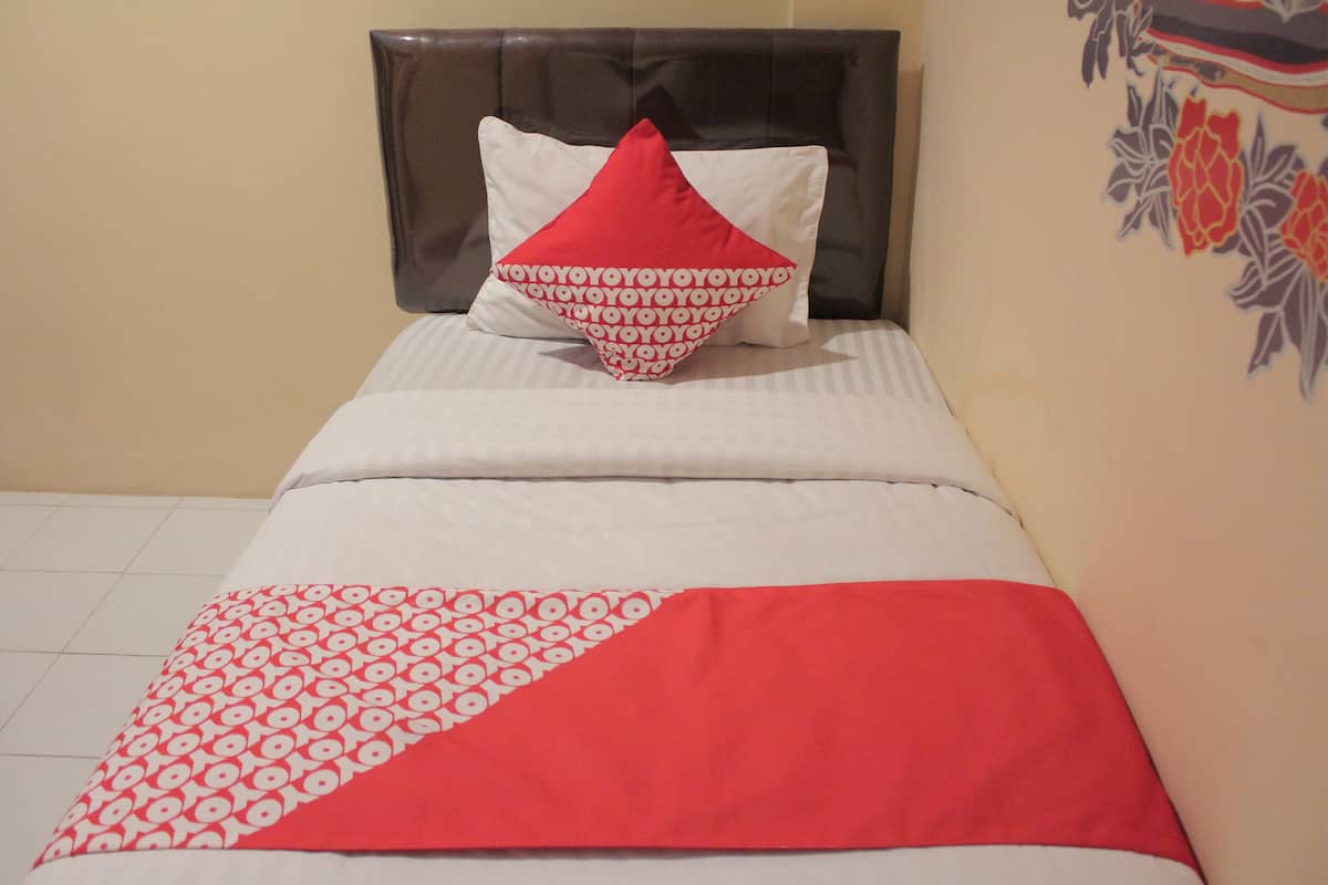 Ein Bett mit einer weiß-rot gemusterten Bettdecke, einem roten und weißen Kopfkissen und einem braunen Kopfteil.