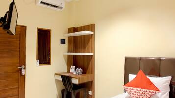 A hotel room with a wooden desk, a bed with a red pillow, and a TV mounted on the wall.