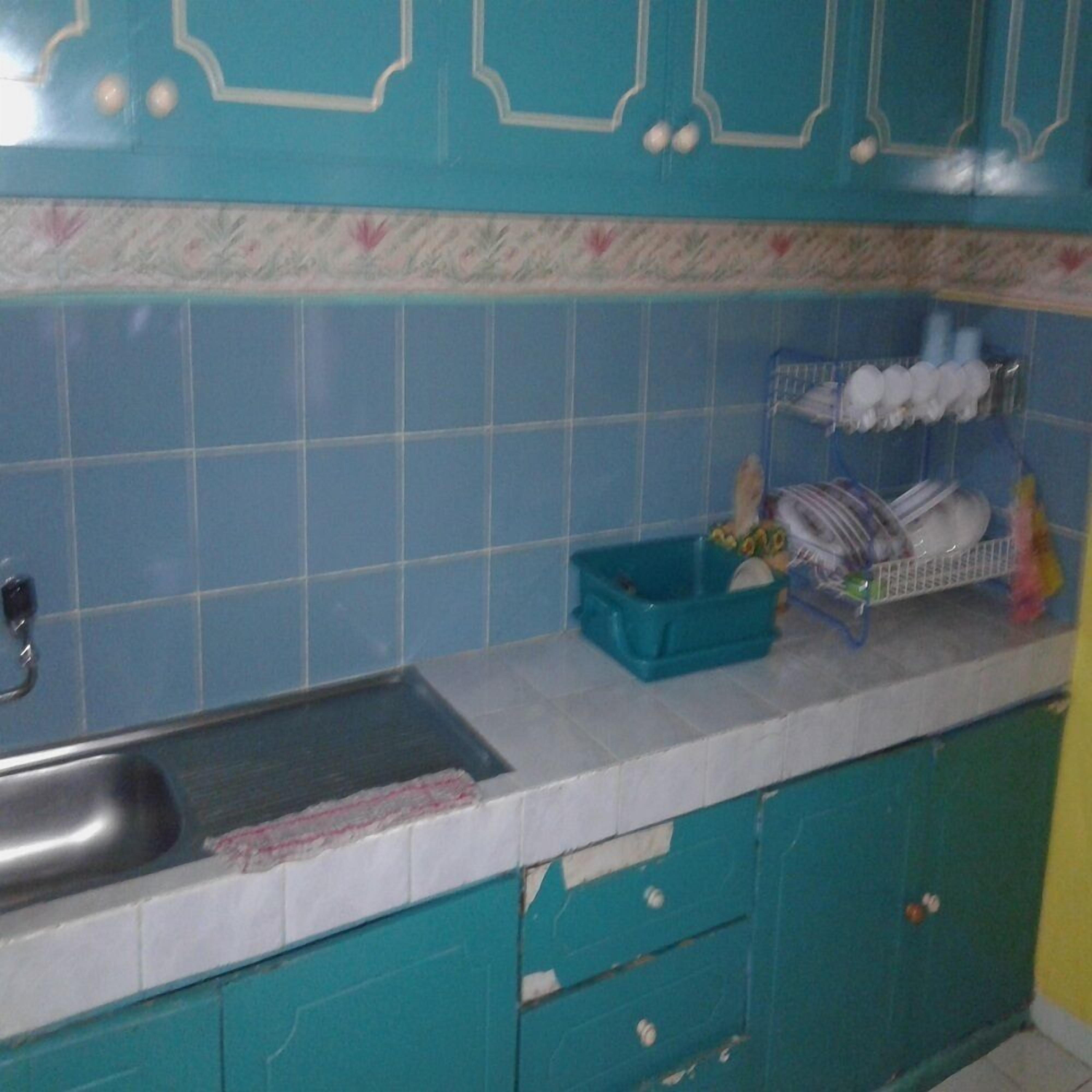A kitchen with teal cabinets, a sink, and a dish rack on the countertop.