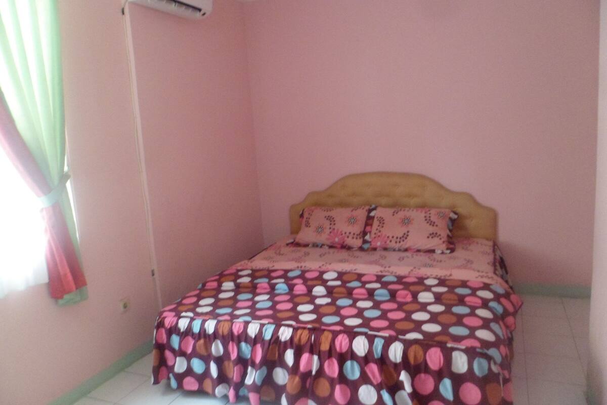 Un dormitorio con cama, ventana con cortinas y un equipo de aire acondicionado en la pared.