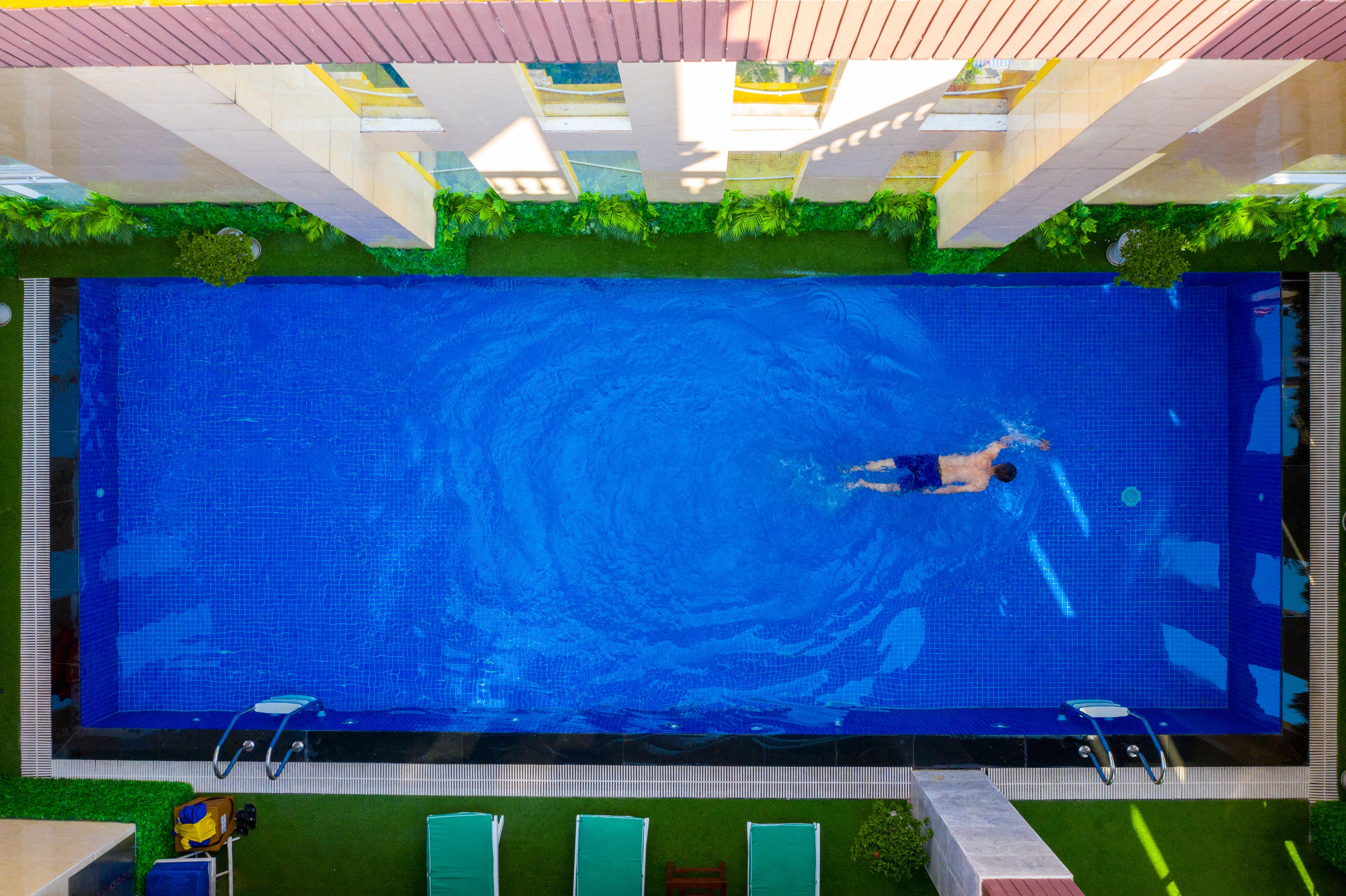 A swimming pool with a person swimming, surrounded by green artificial grass and a tiled deck.