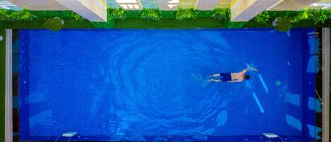 Una piscina con una persona nadando, rodeada de césped artificial verde y una terraza con baldosas.